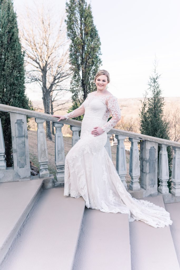 Outdoor bridal portrait on stairs at Stoney Ridge Villa. Bride in long sleeve lace gown from Bliss Bridal.